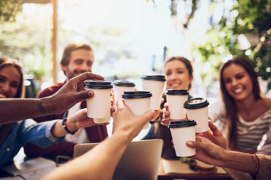 shot of a group of friends toasting with cups of coffee while out together.