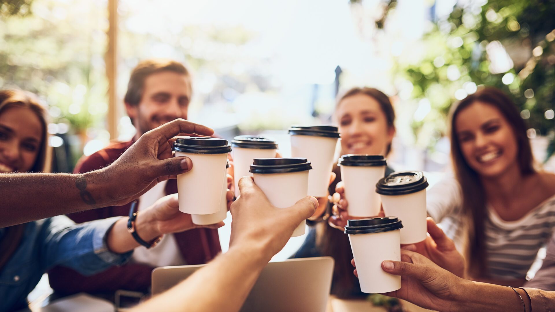 shot of a group of friends toasting with cups of coffee while out together.